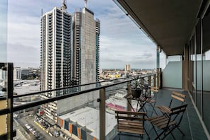 Un balcone con vista su un edificio alto, una pianta in vaso e sedie di legno.