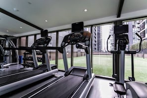A gym with treadmills, ellipticals, and a view of a tennis court through large windows.