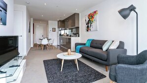 A modern living room with a sofa, a coffee table, a TV, and a kitchen in the background.
