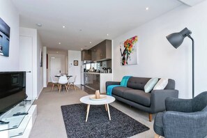 A modern living room with a sofa, a coffee table, a TV, and a kitchen in the background.