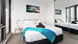 A modern hotel room with a large bed, a small bedside table, a mirror, and a cityscape painting on the wall.