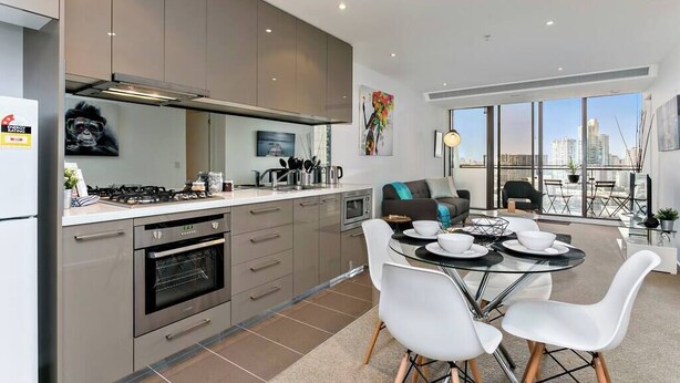 A modern kitchen with a dining area, large windows, and a city view.