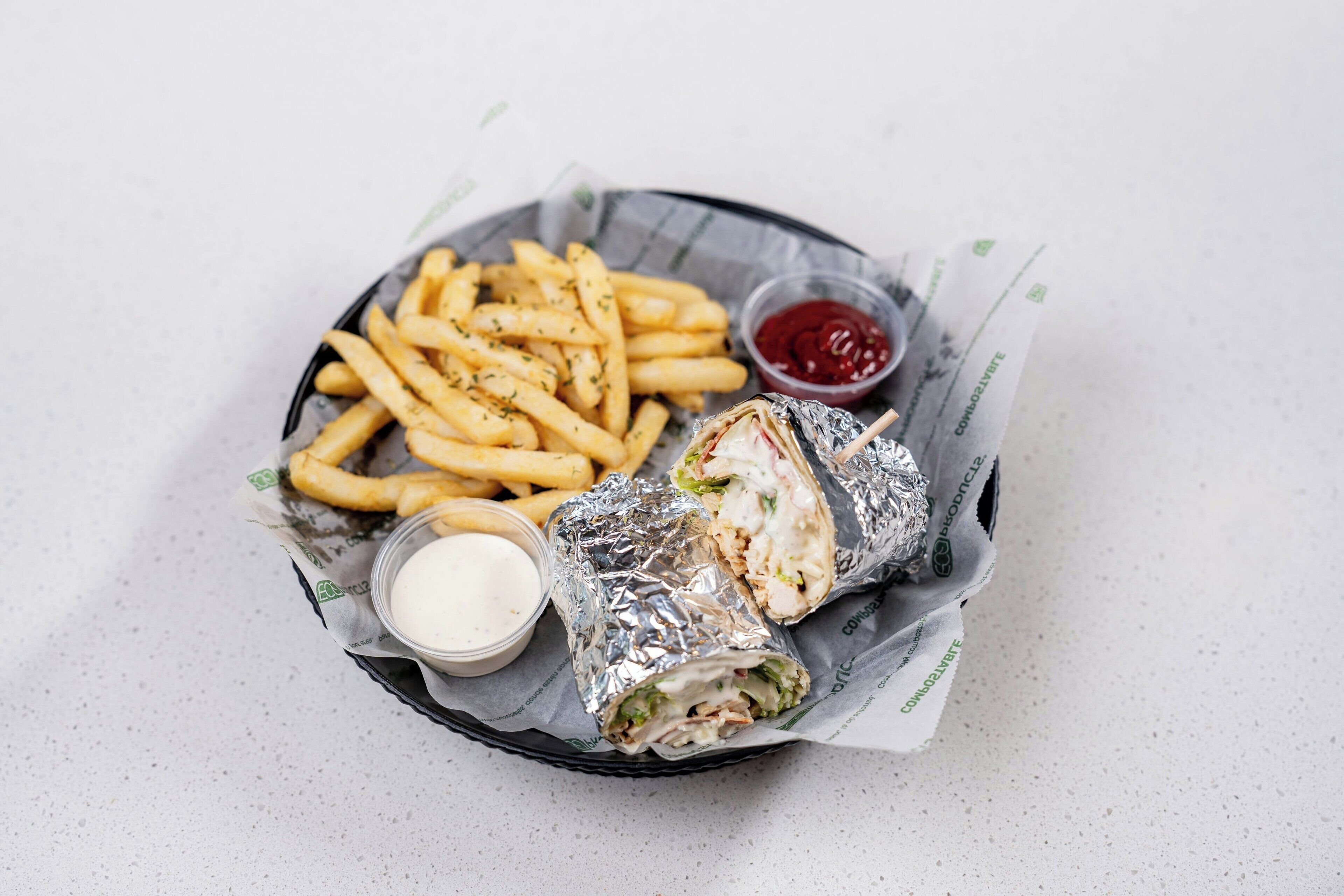 A basket containing a sandwich, fries, a small container of sauce, and a drink.