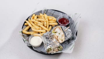 A basket containing a sandwich, fries, a small container of sauce, and a drink.