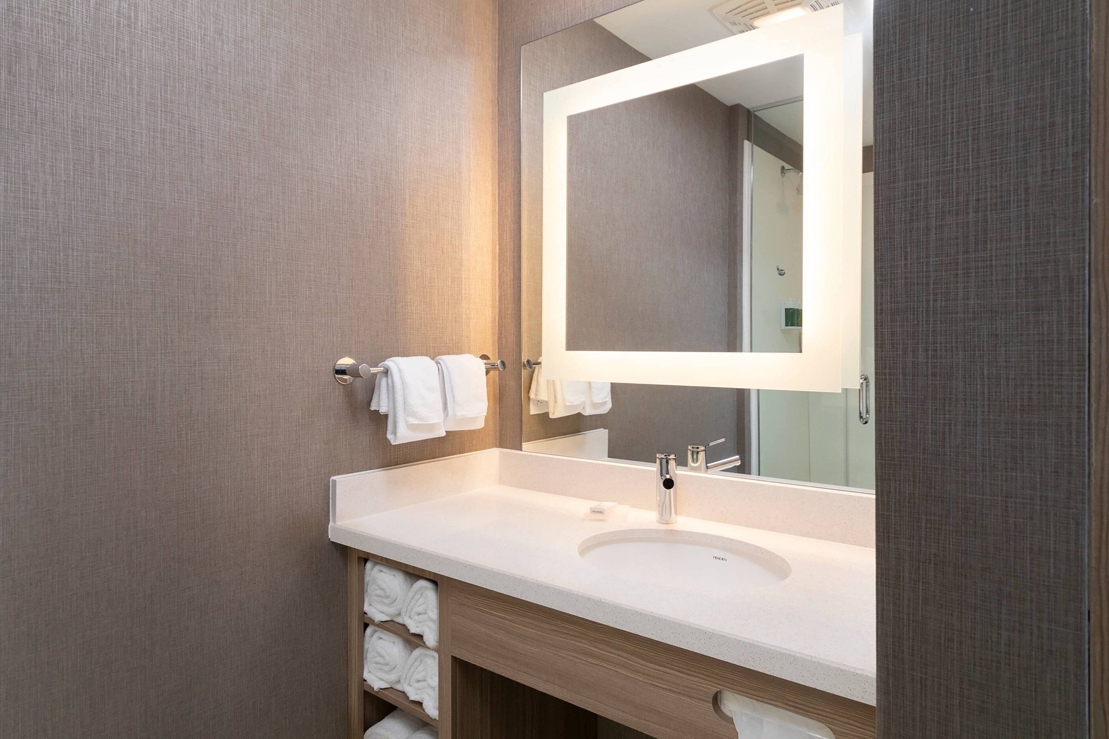 A modern bathroom with a large mirror, white sink, and towel rack.