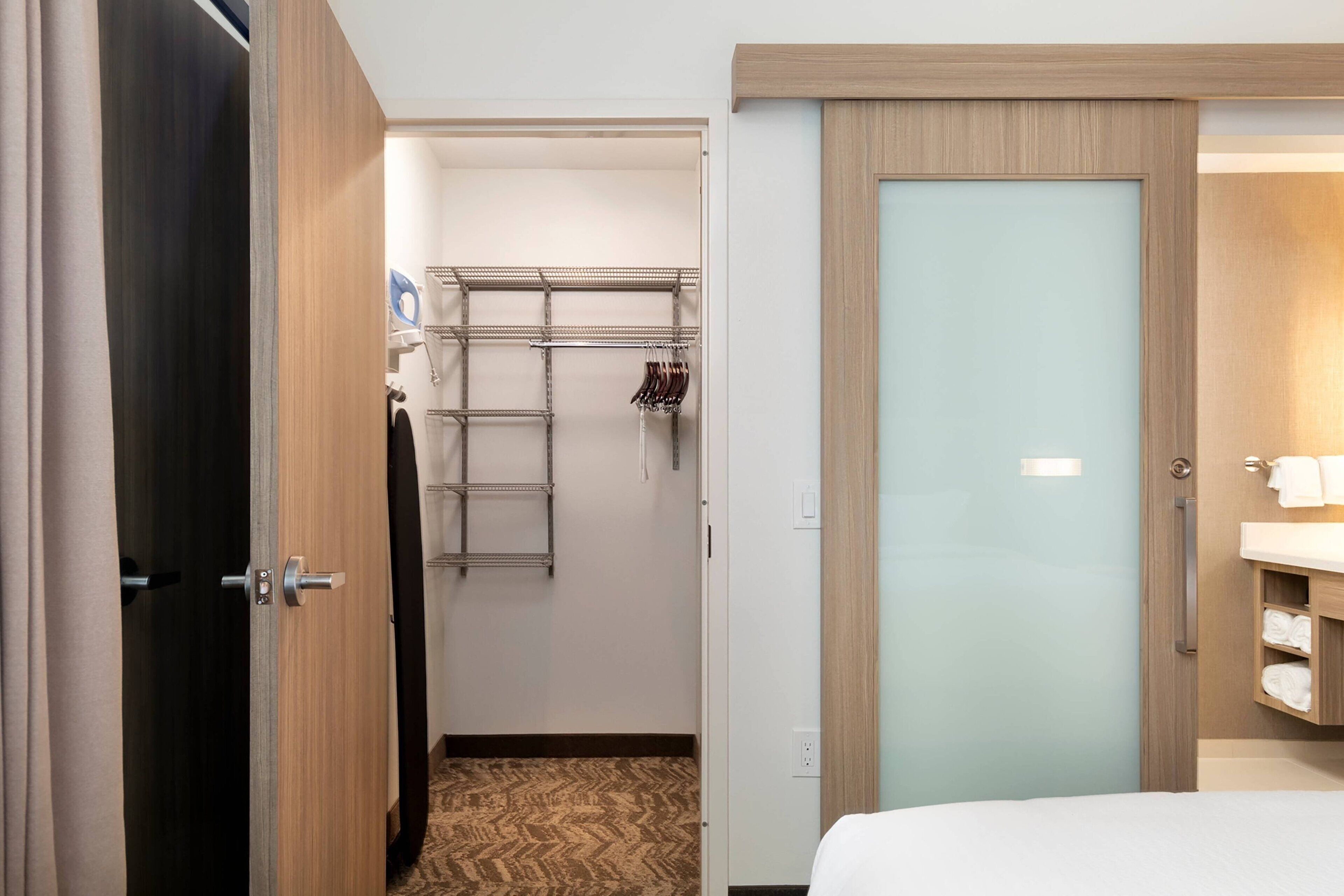 A hotel room with a bed, a bathroom with a sink, and a walk-in closet with shelves and hanging items.
