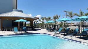 A swimming pool with lounge chairs and umbrellas, a lifeguard station, and a building with a tiled roof. - SpringHill Suites by Marriott Cape Canaveral Cocoa Beach (Cape Canaveral)