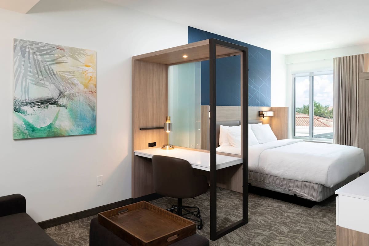 Quarto de hotel com cama, escrivaninha, cadeira e um espelho grande.
