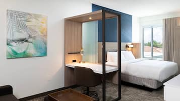A hotel room with a bed, desk, chair, and a large mirror.
