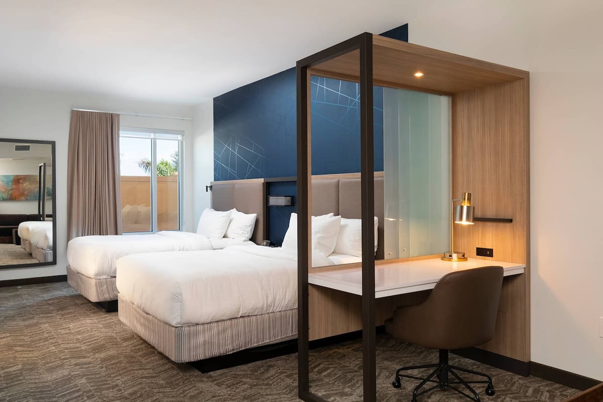 Quarto de hotel com duas camas, uma escrivaninha e uma cadeira.