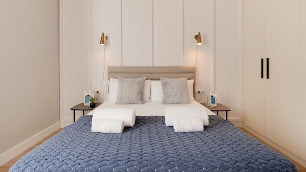 A bedroom with a large bed, two bedside tables, a headboard, and wall-mounted lights.