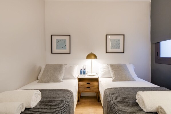 Une chambre double avec deux lits, une table de chevet avec une lampe et deux tableaux encadrés au mur.