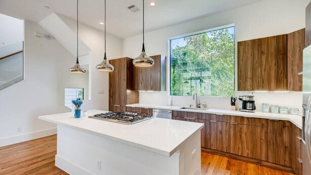 A modern kitchen with a large island, wooden cabinets, pendant lighting, and a view of greenery outside. - Mins To DT Houston / 4-Story/ 7 Beds / City Views

 (Houston)