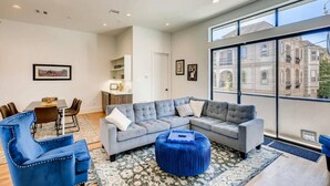 A modern living room with a grey sectional sofa, blue armchairs, and a matching ottoman. A dining area with a table and chairs is visible in the background. - Mins To DT Houston / 4-Story/ 7 Beds / City Views

 (Houston)