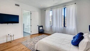 A modern bedroom with a large bed, a flat-screen TV, and a view of the city through the window. - Mins To DT Houston / 4-Story/ 7 Beds / City Views

 (Houston)