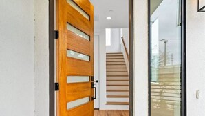 A hallway with a wooden door, a staircase, and a glass door leading to an outdoor area. - Mins To DT Houston / 4-Story/ 7 Beds / City Views

 (Houston)