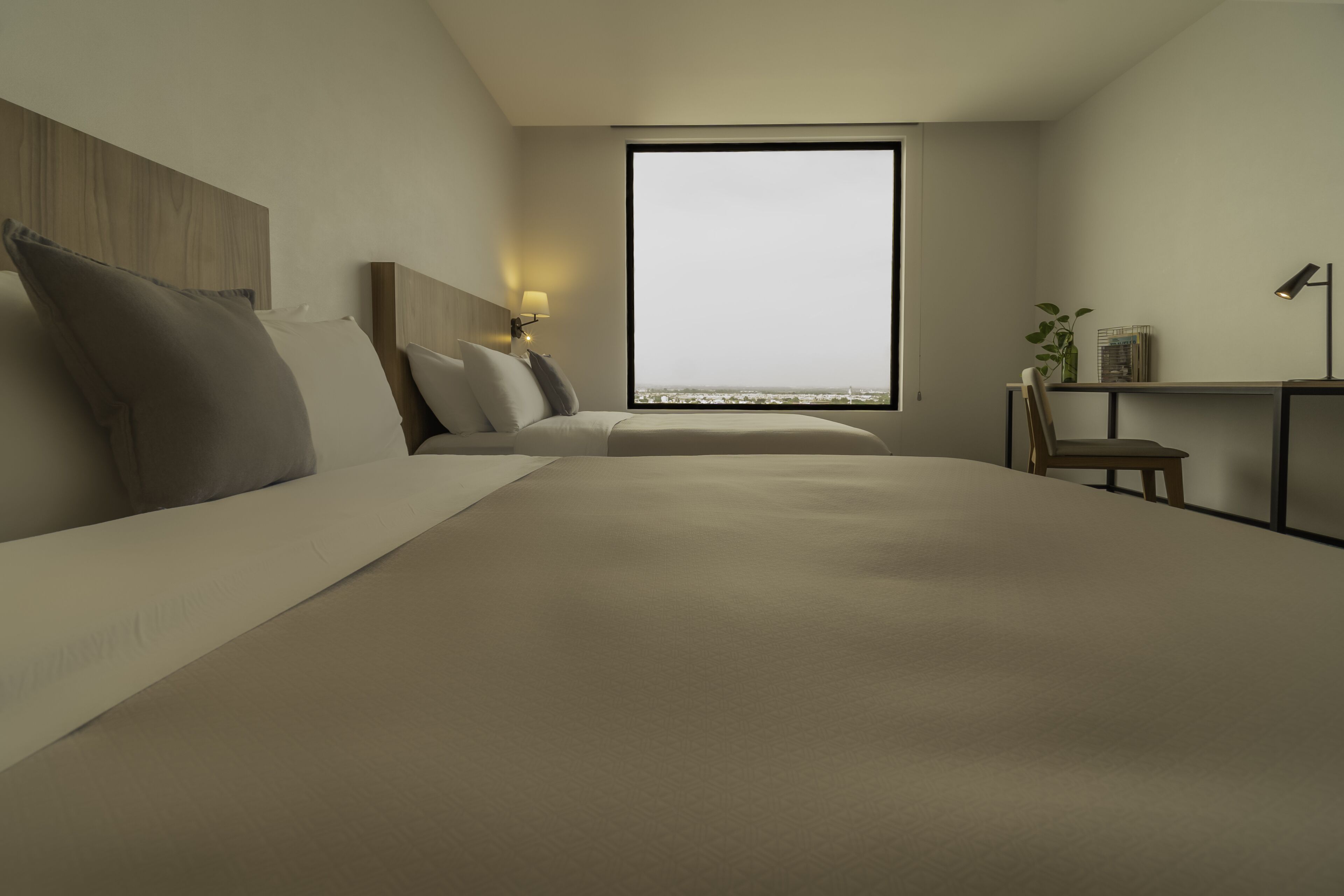A modern hotel room with a large bed, a desk with a chair, a small table, and a large window offering a view.