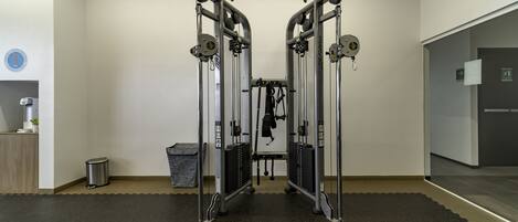 Une salle de sport équipée de deux appareils d’exercice fixés au mur, dotés de miroirs, d’une petite poubelle et d’une porte donnant sur une autre pièce.