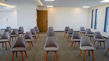 Un salón de conferencias con hileras de sillas grises de patas de madera, piso alfombrado, paredes blancas y una puerta de madera.