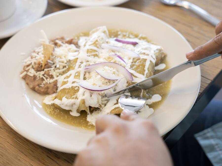 A plate of enchiladas with cheese and onions being cut with a knife.