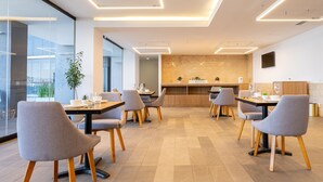 A modern dining area with grey upholstered chairs, wooden tables, and a central island with a kitchen counter. -  Stadía Suites Querétaro Centro Histórico (Querétaro)