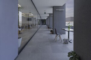 Un espacio de oficina moderno con paredes de vidrio, filas de mesas y sillas, y plantas en macetas.