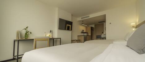 Een hotelkamer met een groot bed, een bureau, een stoel, een kleine tafel met een plant, een spiegel en een kitchenette op de achtergrond.