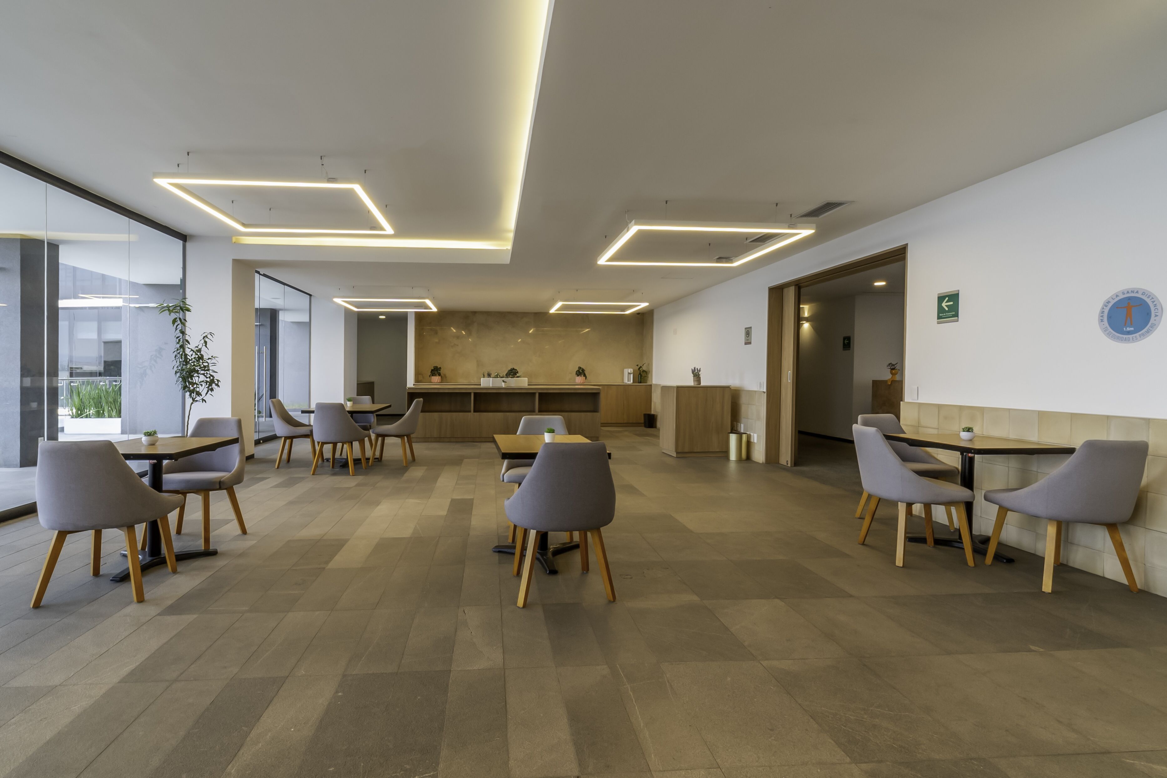 Una sala de conferencias moderna con luces de techo rectangulares, una mesa central con sillas y una zona de cocina al fondo.