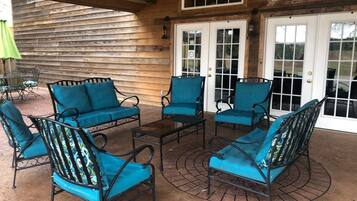 A covered patio area with four blue cushioned chairs and a small table, wooden walls, and a large window with a view of the outdoors.