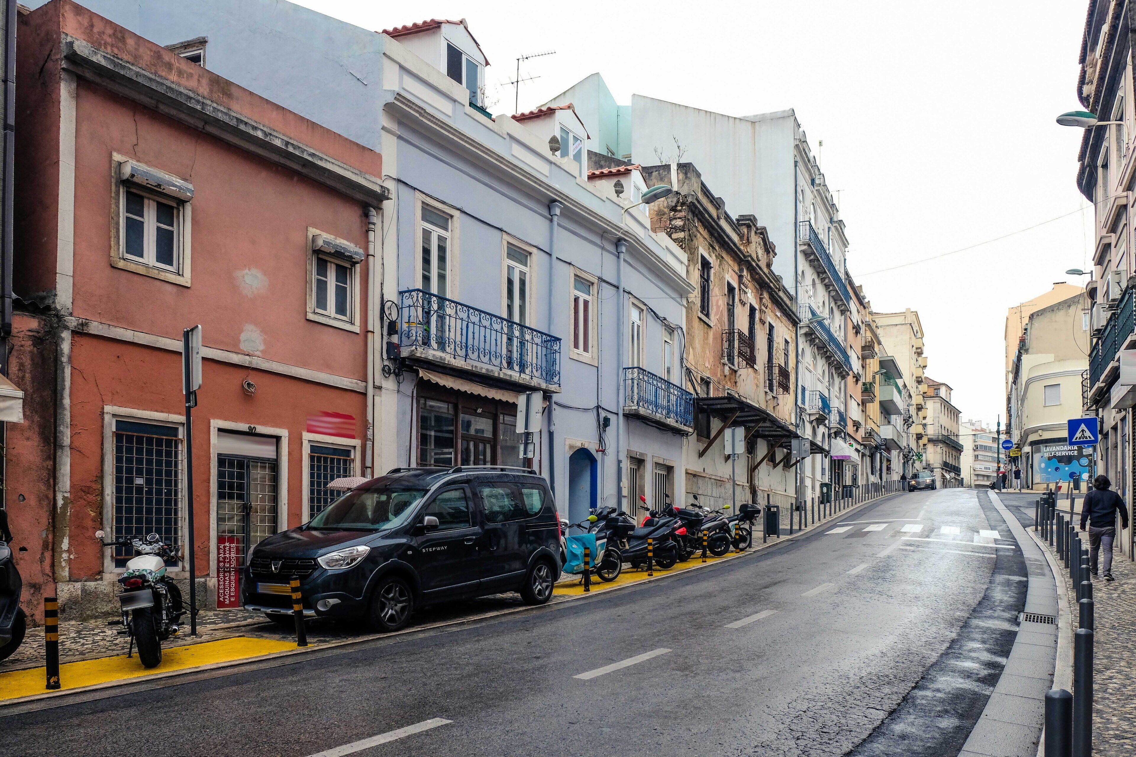 Una calle flanqueada por edificios de varios pisos, coches aparcados y motocicletas.