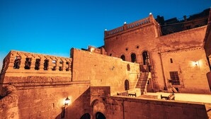 A historic stone building with arched doorways and a staircase leading to an upper level. - Maristan Tarihi Konak (Mardin)