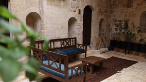 A stone-walled room with a wooden bench and a small table, a tiled floor, and a patterned rug. - Maristan Tarihi Konak (Mardin)