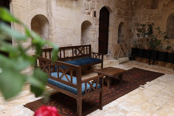 A stone-walled room with a wooden bench and a small table, a tiled floor, and a patterned rug.