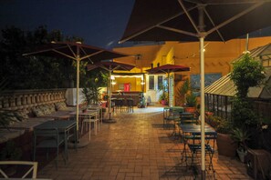 An outdoor patio area with tables and chairs, umbrellas, and potted plants.