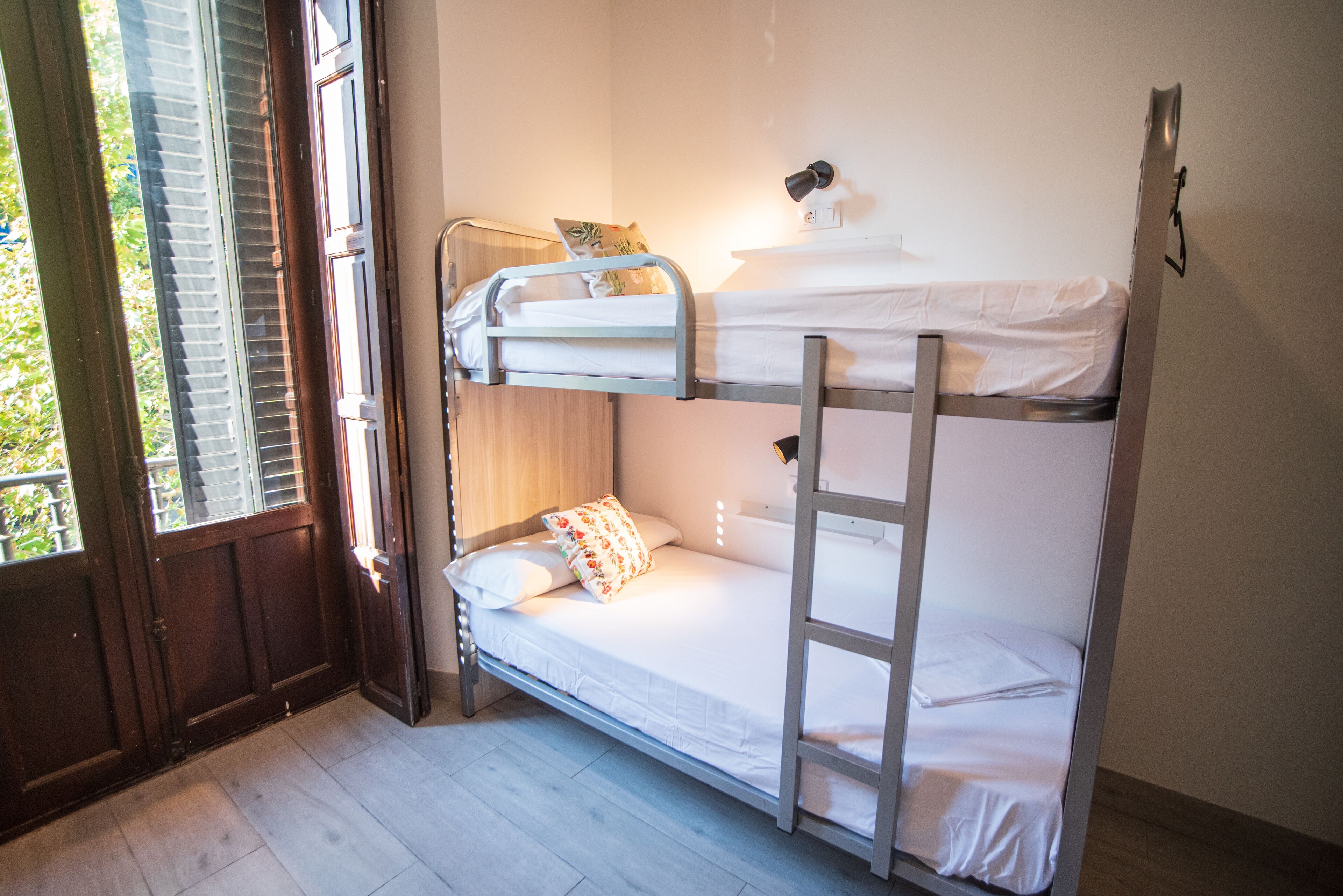 A bunk bed room with a wooden door, a window with blinds, and a wall-mounted light.