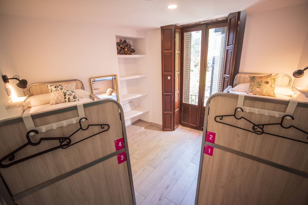 Hotellihuone, jossa on kaksi sänkyä, puulattia, pieni hylly koriste-esineille ja liukuovi, joka johtaa parvekkeelle.