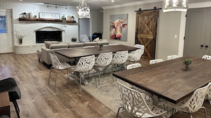 A spacious dining area with a large wooden table and white chairs, a fireplace, and a barn-style door. - Lyric Retreat at GratiDude Ranch - Sleeps 23 with Pool in Leiper's Fork (Franklin)