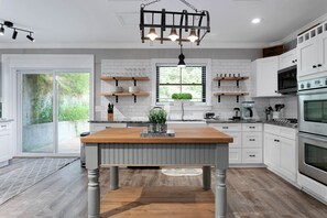 Une cuisine moderne avec des meubles blancs, un îlot central en bois et un luminaire suspendu.