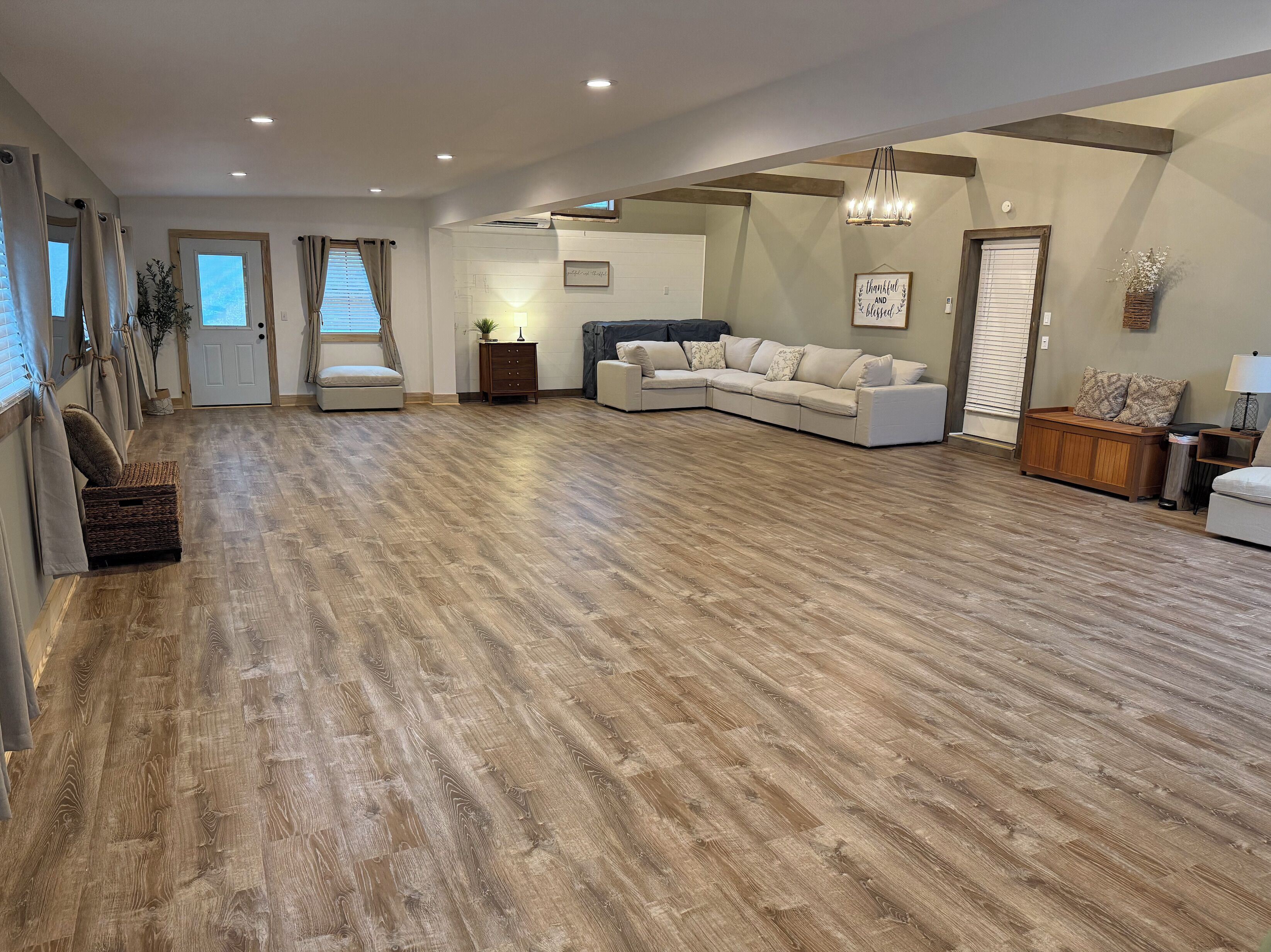 Un salon spacieux avec un grand canapé d’angle, un plancher en bois et un lustre.