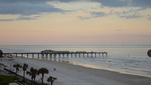 A beach with a pier extending into the ocean, a pool area, and palm trees. - Luxury Ocean View Condo with Access to No Drive Beach (Daytona Beach Shores)