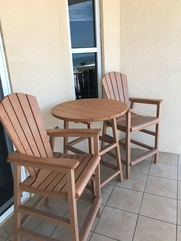A small patio area with two wooden Adirondack chairs and a round table. - Luxury Ocean View Condo with Access to No Drive Beach (Daytona Beach Shores)