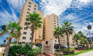 A hotel with a sign reading "Sanibel", surrounded by palm trees and a clear sky.