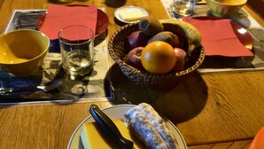 Puinen ruokapöytä on katettu aamiaistarvikkeilla, kuten hedelmäkulholla, lasillisella mehua ja juustolautasella.