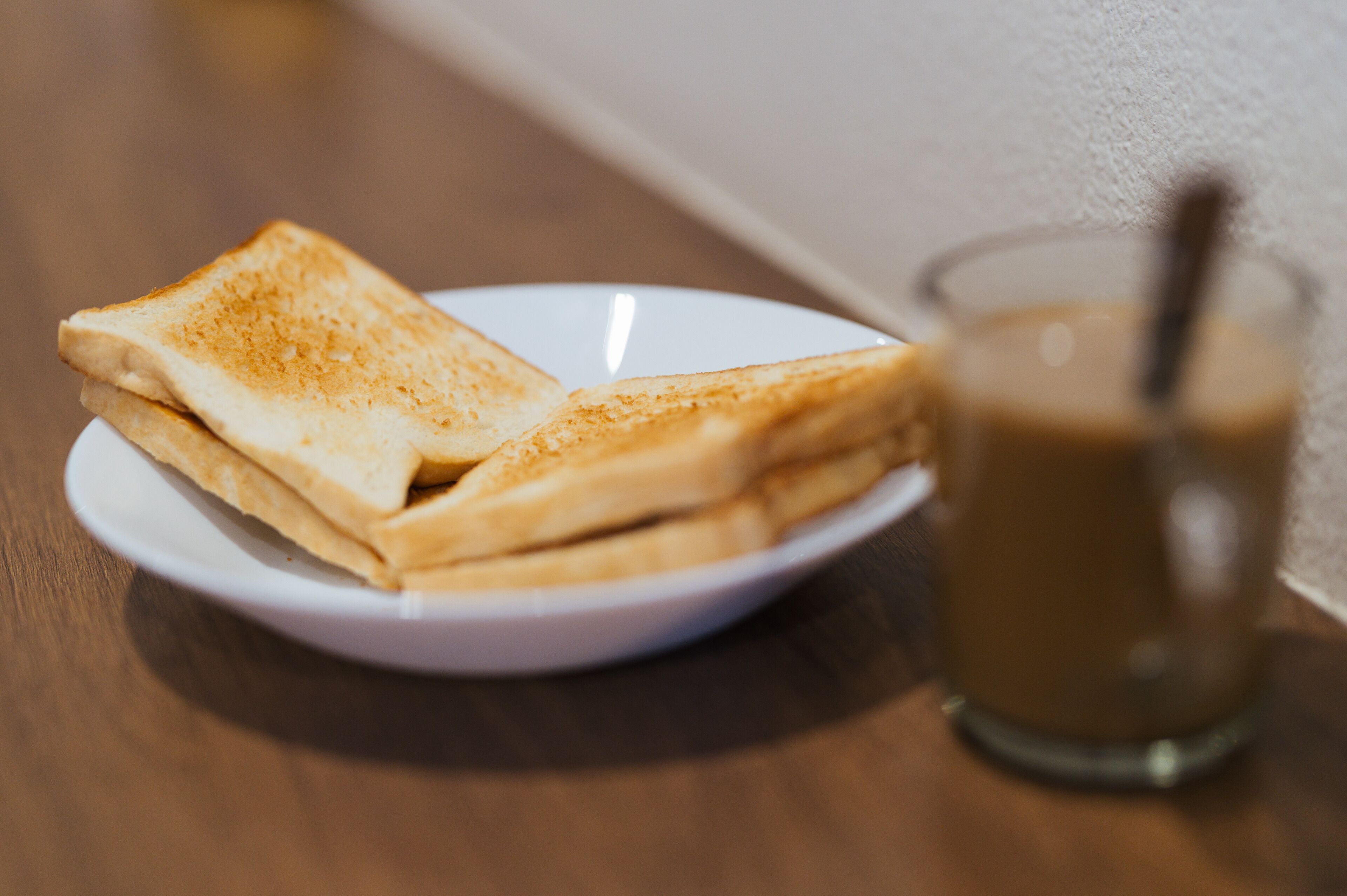 Un plato con dos rebanadas de pan tostado y un vaso de café helado sobre una mesa de madera.