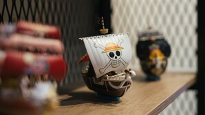 Ein kleines Schiffmodell mit Totenkopf und gekreuzten Knochen auf der Segel, auf einer Holzoberfläche platziert.