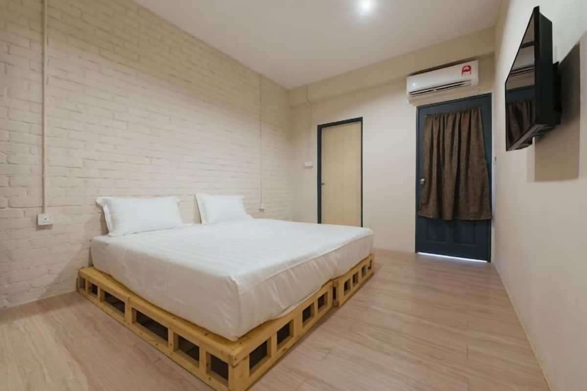 Un dormitorio con cama de palets de madera, pared de ladrillo blanco, una puerta con cortina y un equipo de aire acondicionado.