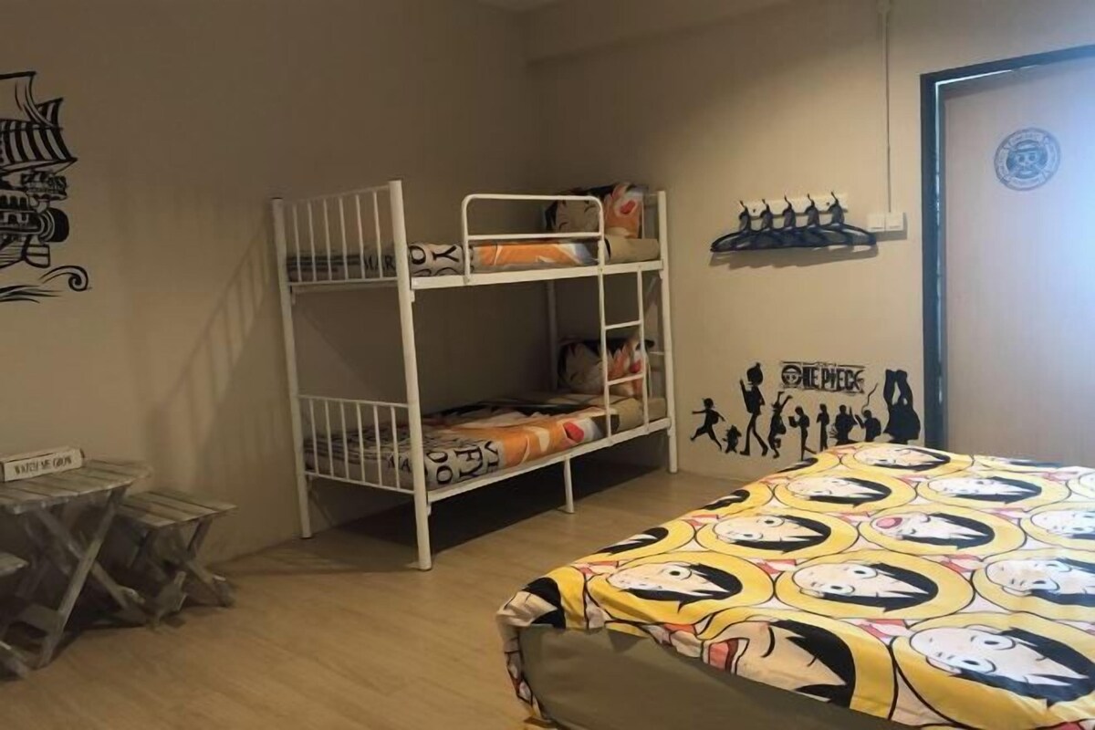 Une chambre avec un lit superposé, un lit situé à l’extrémité, une petite table et un mur orné d’une affiche.