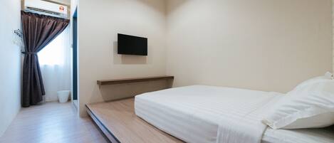 A bedroom with a bed, a mounted TV, a window with curtains, and an air conditioning unit.