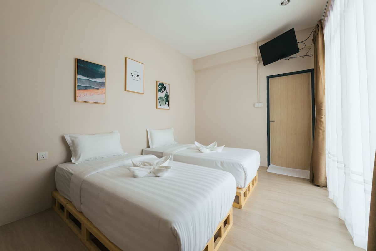 Habitación de hotel con dos camas, un televisor montado en la pared y una puerta con cortina.