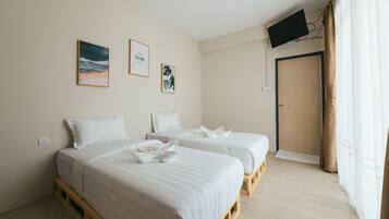 A hotel room with two beds, a television mounted on the wall, and a door with a curtain.
